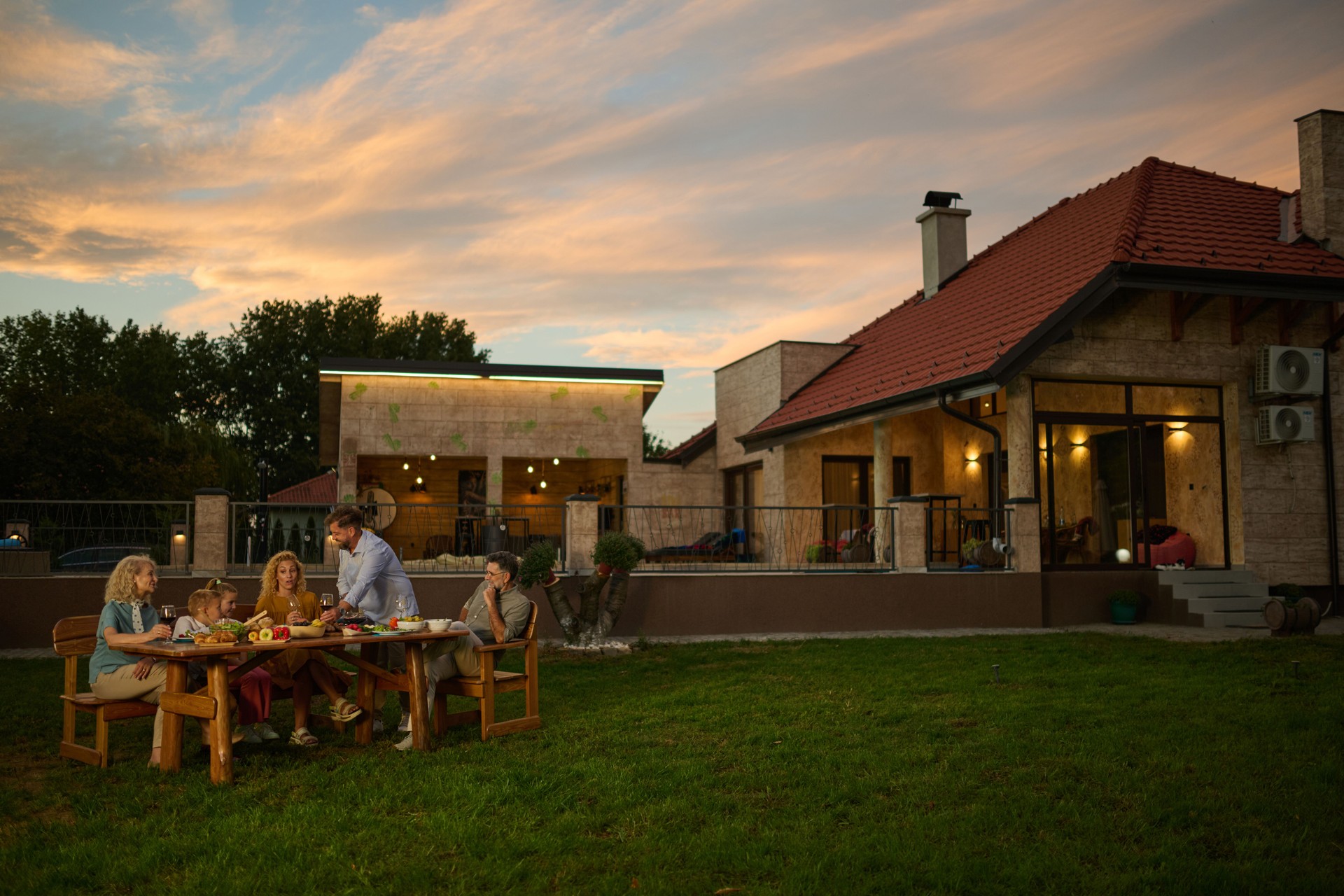 Family enjoying dinner together at sunset in backyard of modern home